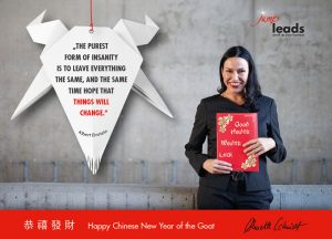 Glückwunschkarte zum chinesischen Neujahr: in der linken Bildhälfte eine Origami-Ziege aus weißem Papier mit dem Zitat von Albert Einstein über Veränderungen. In der rechten Bildhälfte eine dunkelhaarige, lachende Frau im schwarzen Anzug, die eine rote Mappe vor sich hält mit guten Wünschen wie Gesundheit, Wohlstand und Glück.