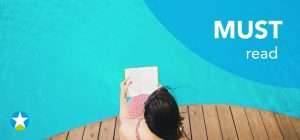 Frau sitzt am Poolrand aus Holz und lässt ihre Beine im Pool kühlen. Dabei liest sie ein Buch. Aus der Vogelperspektive fotografiert.