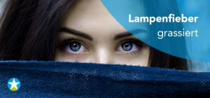 Eine dunkelhaarige Frau mit grünen Augen verbirgt Nase und Mund hinter einem blauen Stoff. Nur ihre Augen sind sichtbar.