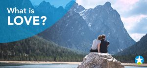 Ein junges Pärchen, von hinten fotografiert, sitzt auf einem Felsen in einer Berglandschaft und schaut auf den See vor ihnen. Sie haben ihre Köpfe aneinander gelegt.