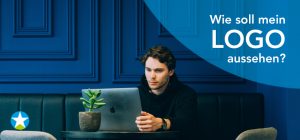 Junger Mann im schwarzen Hoodie sitzt mit einem Laptop auf einer schwarzen Ledercouch. Im Hintergrund eine dunkelblaue Holzpanel-Wand. Auf dem Tisch vor ihm eine Sukkulente. Er schaut konzentriert auf den Bildschirm.